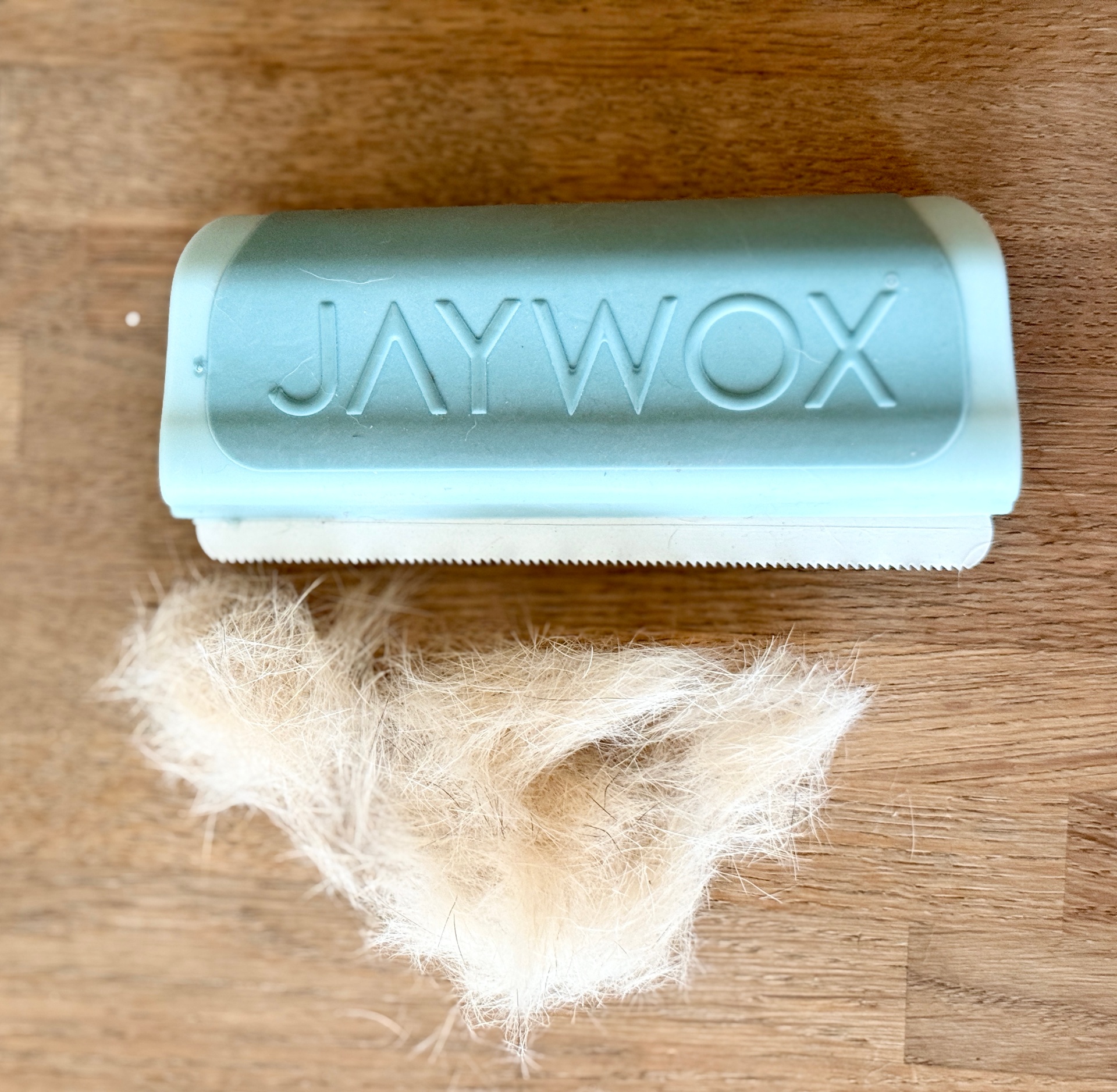JAYWOX fällningskam i Blue Mist på trägolv bredvid en stor uppsamlad hög av ljus underull efter ett pass på hund